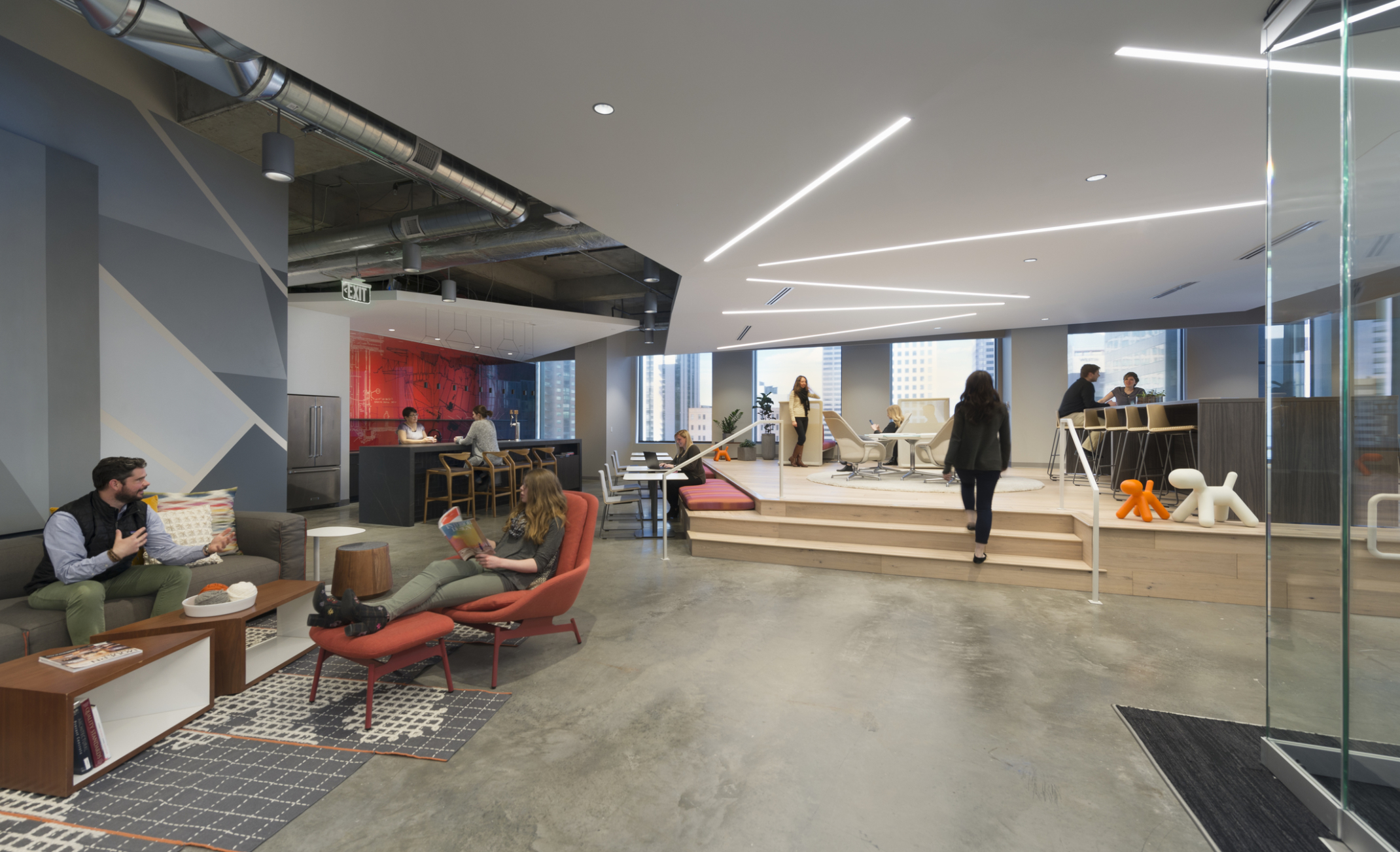 open design studio with step up to wood platform with flexible seating, local artist work on walls, and concrete flooring