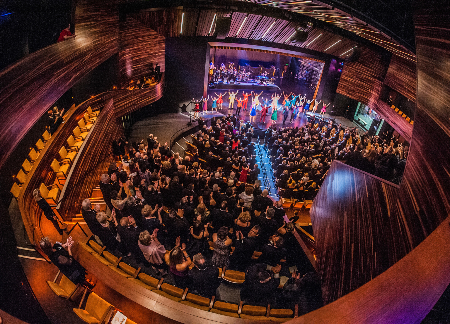 fisheye view of theater with audience and cast bowing on stage, surrounded by dark wood paneling and deep purple lights fisheye view of theater with audience and cast bowing on stage, surrounded by dark wood paneling and deep purple lights
