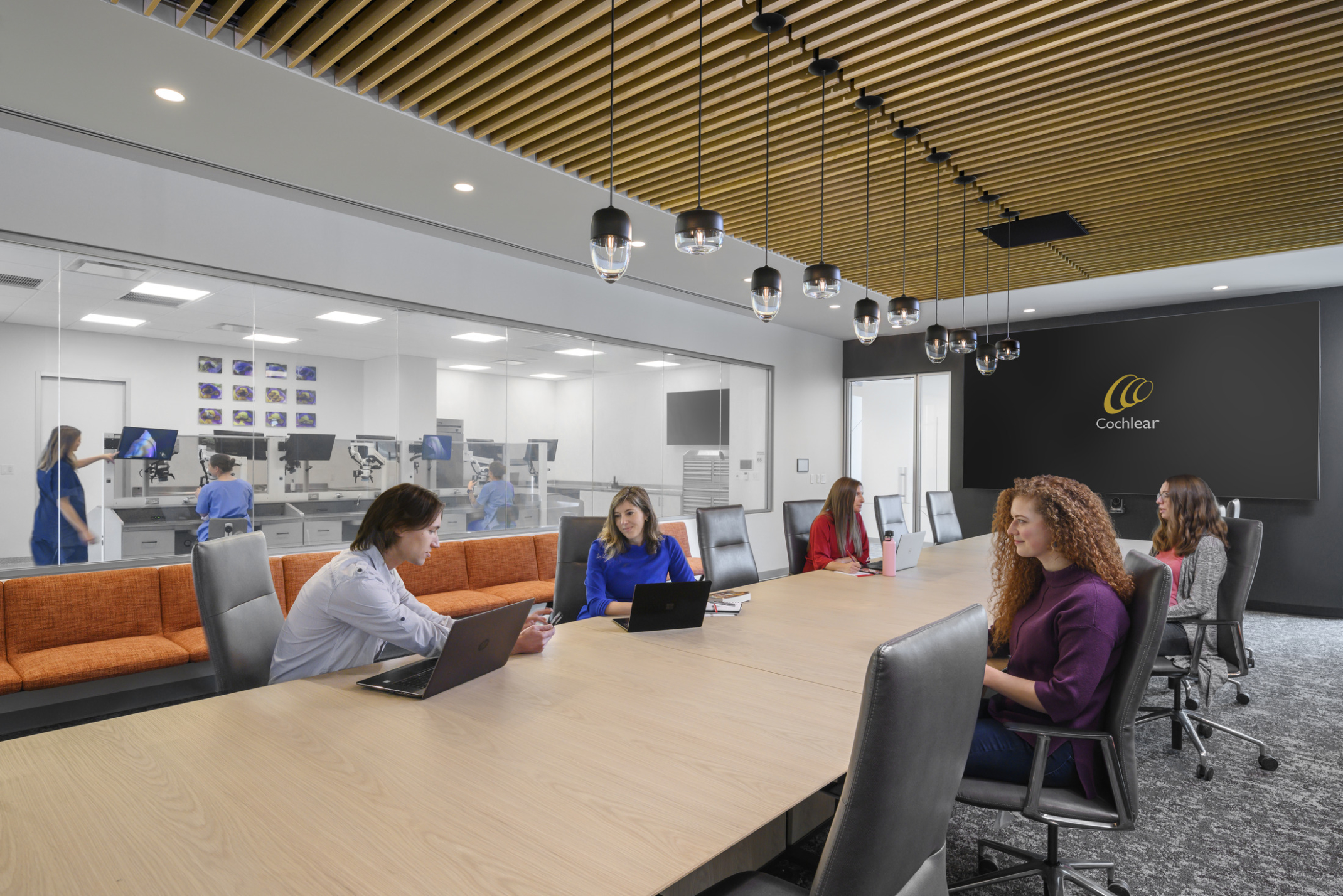 diverse group of people sitting around a conference table with wood acoustic panels above, glass walls out to working area, and orange seating