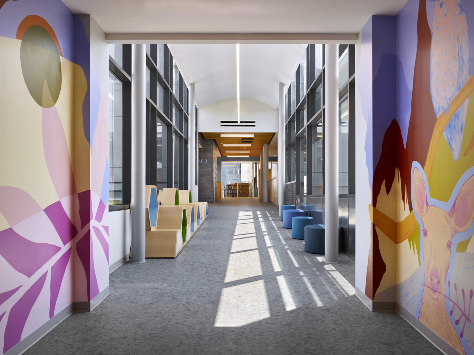 Colorful mural walls on both sides of the hallway with flexible seating at Maury Elementary School.