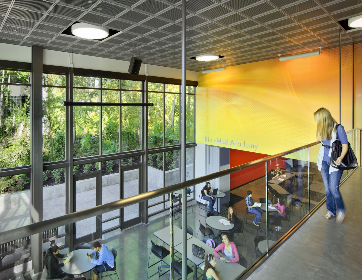 Upper level overlook on dining room with double height, floor to ceiling windows with views to forest at Marysville Getchell High School.