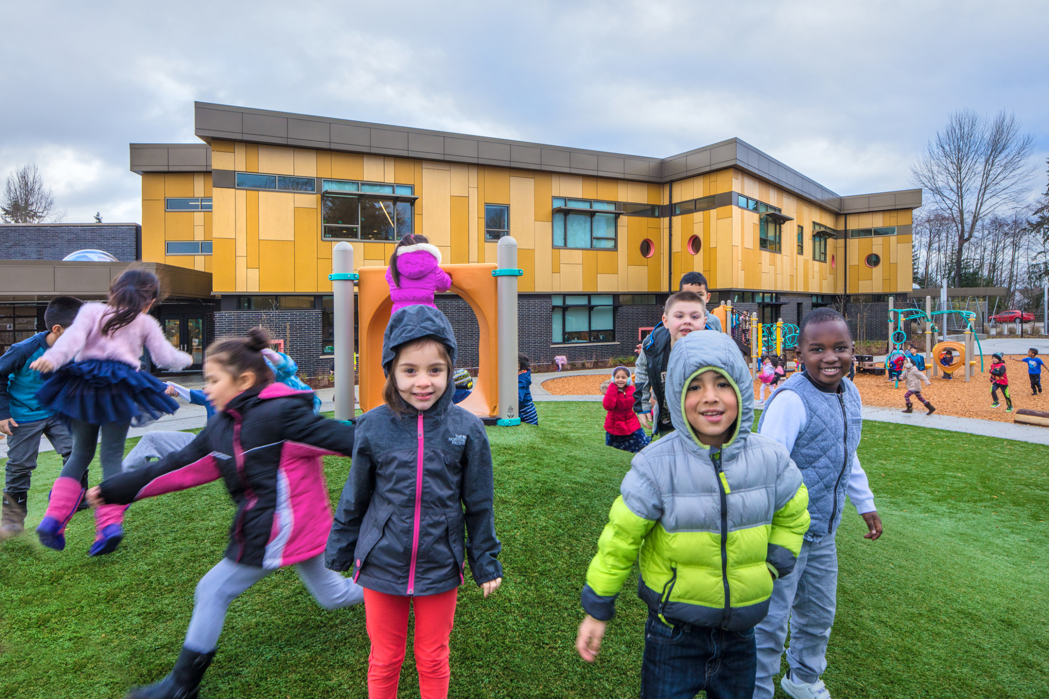 smiling children on a playground outside a yellow kindergarten center smiling children on a playground outside a yellow kindergarten center