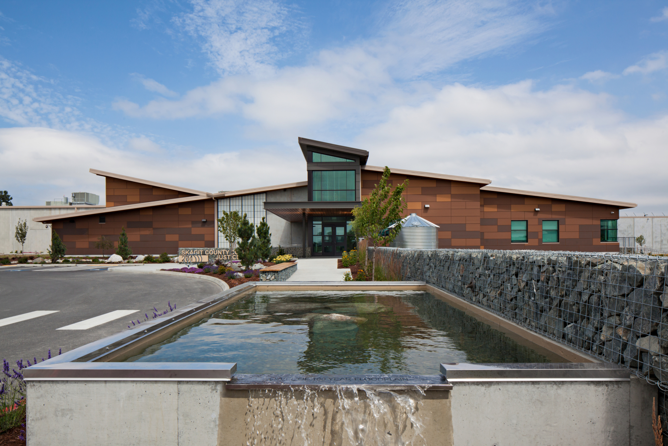a water feature next to a stone gabion in front of a stone and glass building a water feature next to a stone gabion in front of a stone and glass building