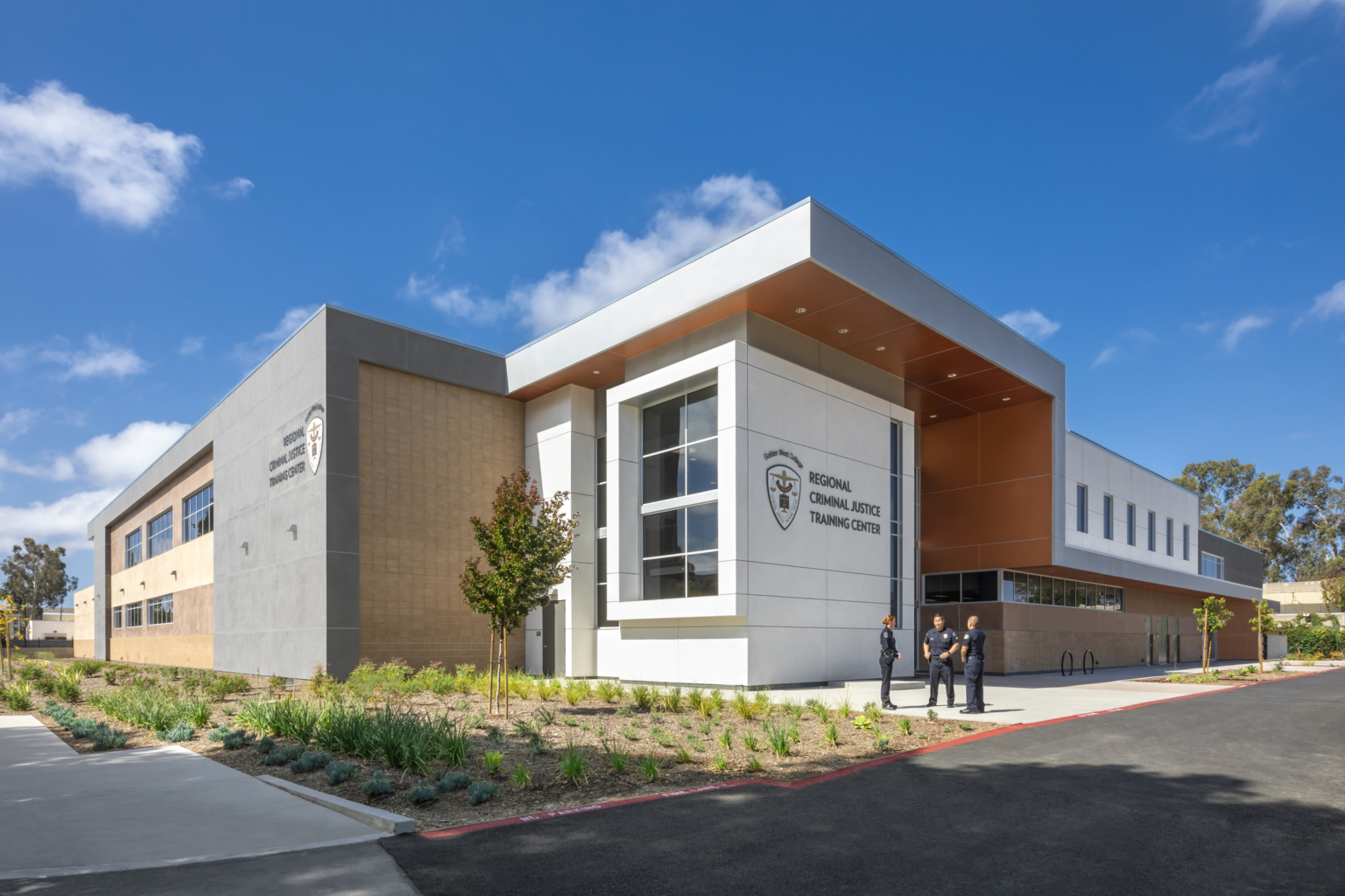 Font entryway with varying building heights, large windows, orange, white, and grey facade at Golden West College Criminal Justice Training Center Font entryway with varying building heights, large windows, orange, white, and grey facade at Golden West College Criminal Justice Training Center