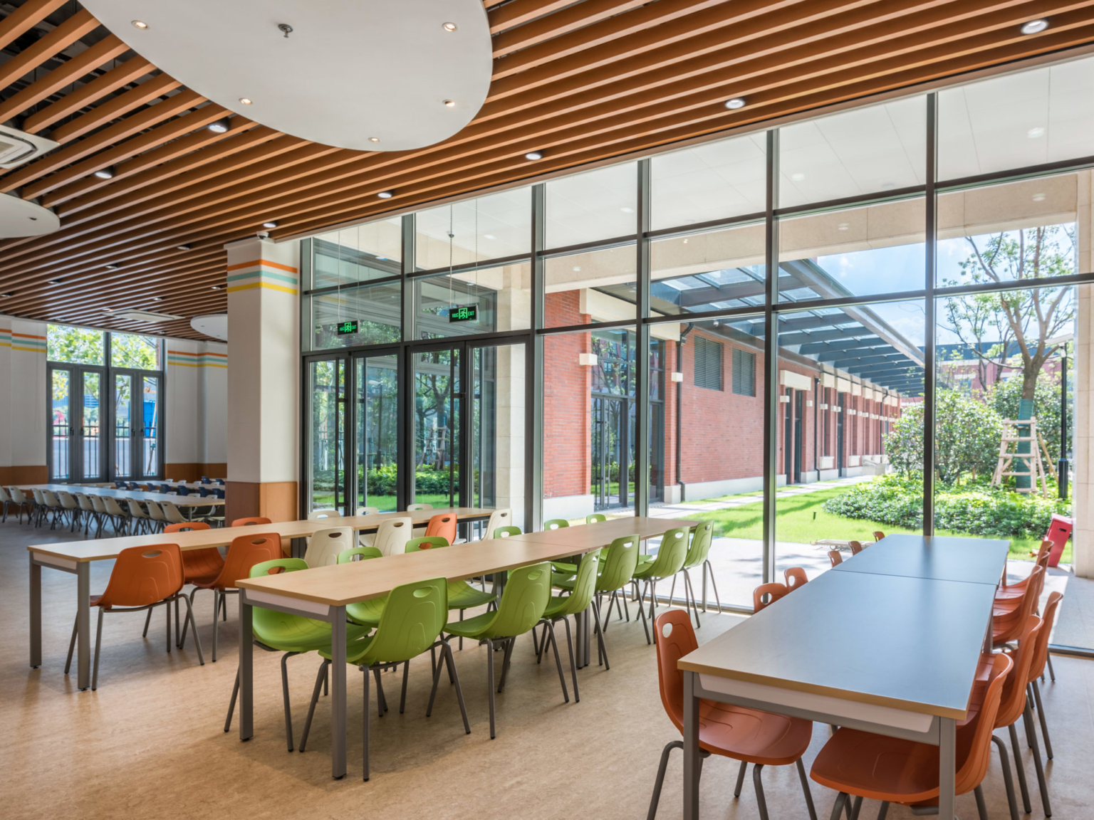 orange and green chairs at long tables next to a large open window at Huili International School