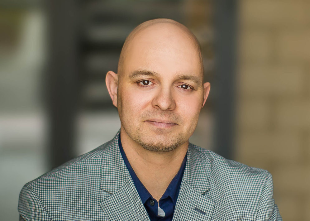 grinning man with a gray suit jacket and dark button up shirt