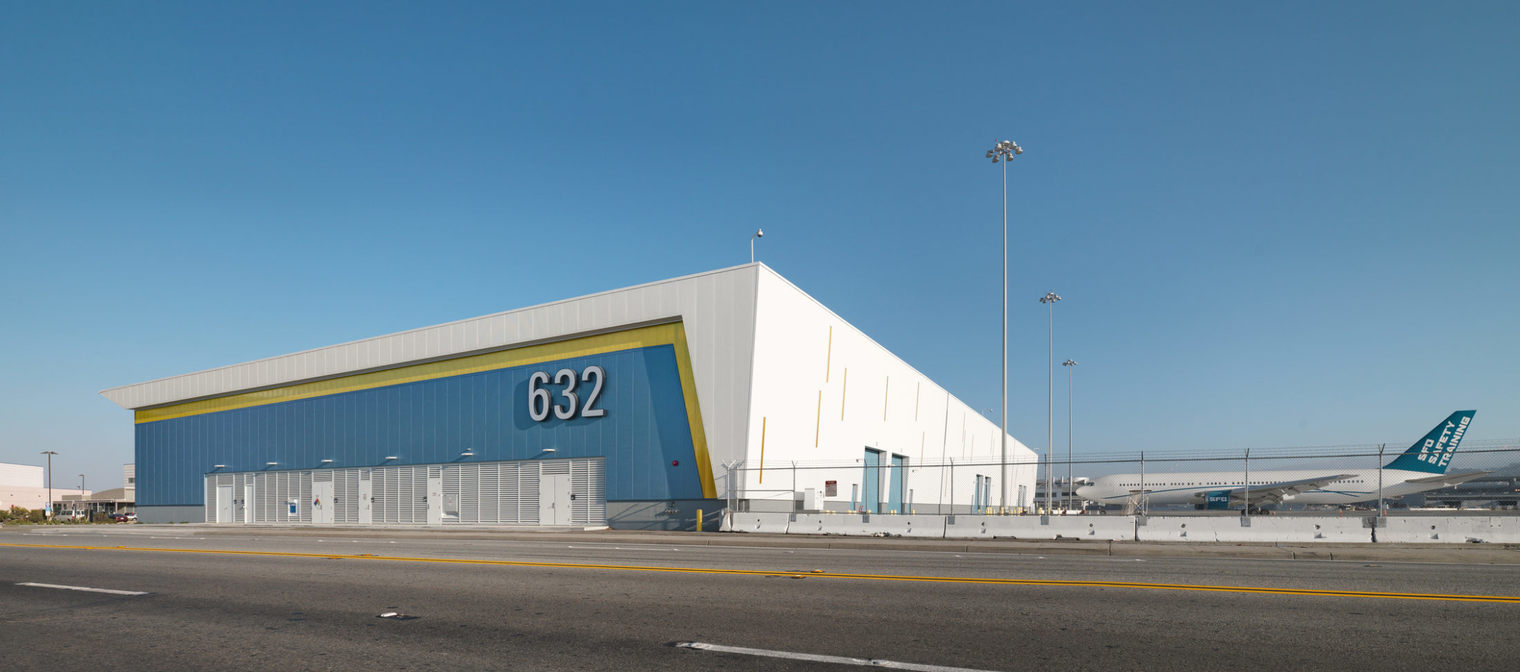 exterior view of blue yellow and white cargo building at airfield with airplane and blue sky exterior view of blue yellow and white cargo building at airfield with airplane and blue sky