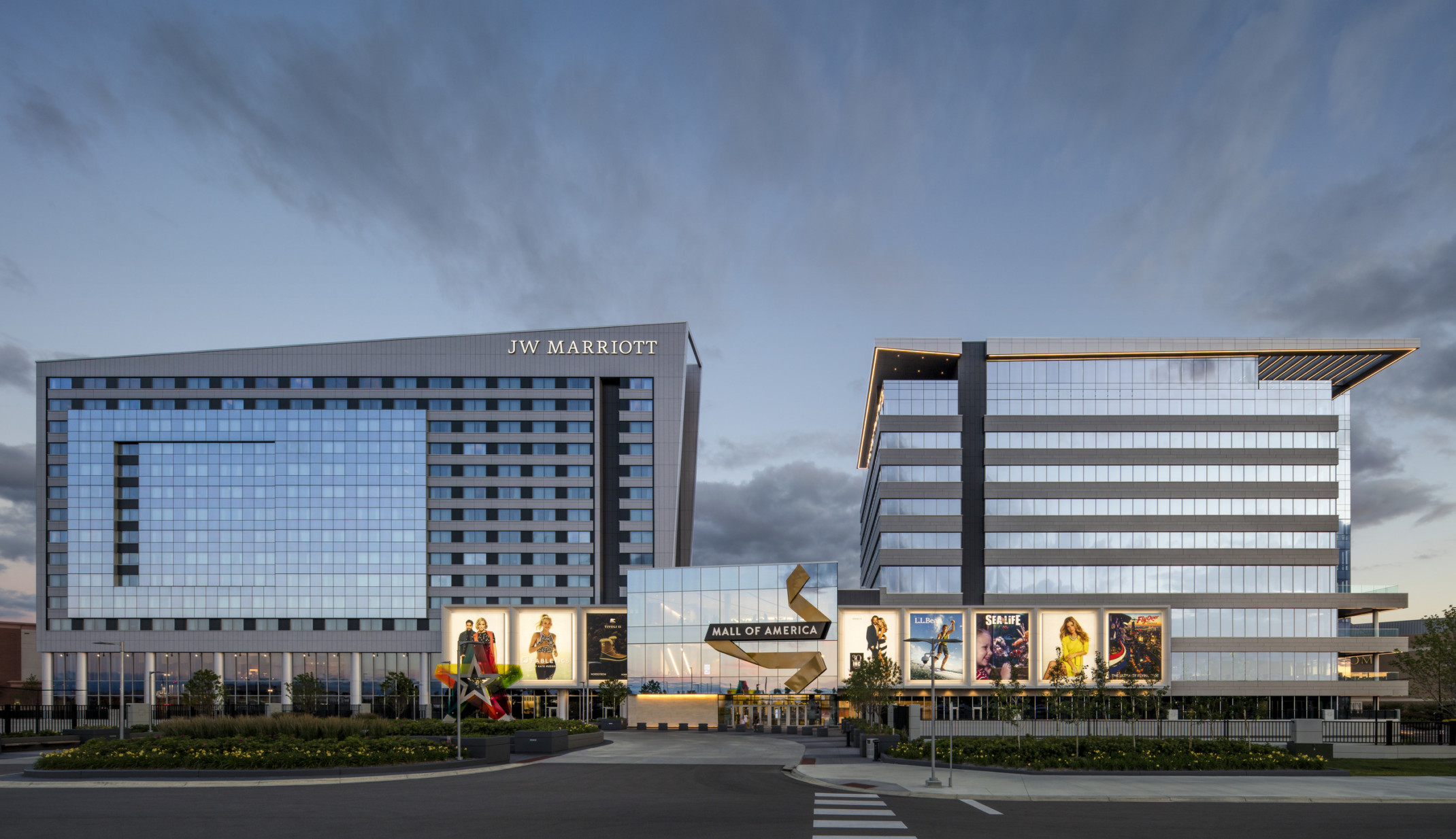 two modern glass buildings connected by a glass cube with large advertising billboards in front