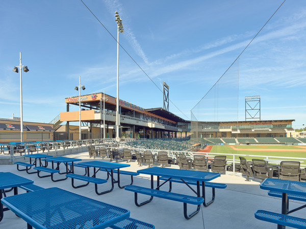 View from behind right field looking toward the stadium seating from alternative seating area that includes blue picnic tables and swivel chair seating. View from behind right field looking toward the stadium seating from alternative seating area that includes blue picnic tables and swivel chair seating.