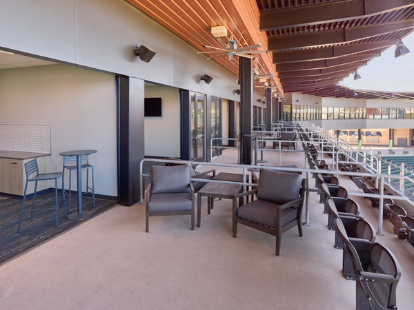 View from premium suites with open interior room on the left and patio with outdoor chairs and railings overlooking stadium seating on the right. View from premium suites with open interior room on the left and patio with outdoor chairs and railings overlooking stadium seating on the right.