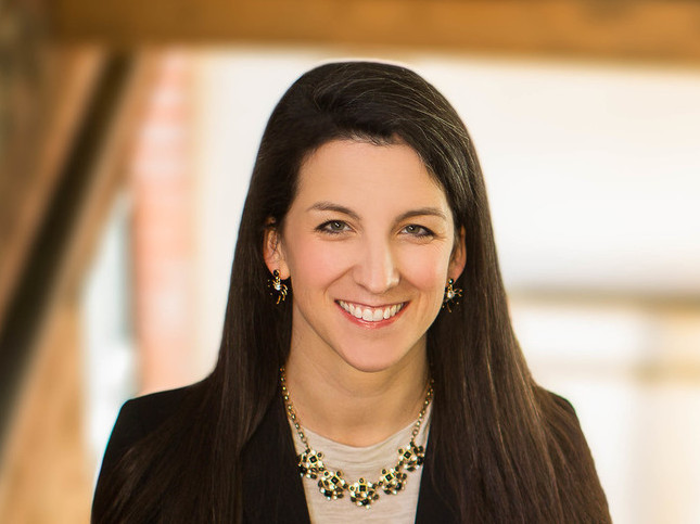 Kate Thuesen in a dark jacket and light shirt standing on a staircase